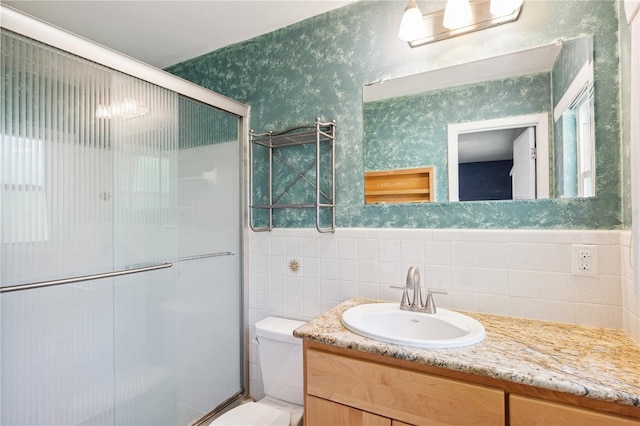 bathroom with tile walls, a shower stall, vanity, toilet, and wallpapered walls
