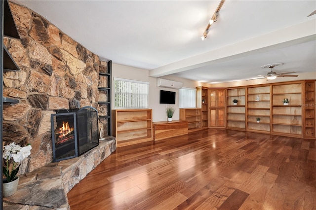 unfurnished living room with an AC wall unit, a ceiling fan, wood finished floors, and a stone fireplace