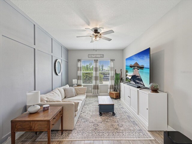 living area featuring a ceiling fan, baseboards, wood finished floors, and a textured ceiling