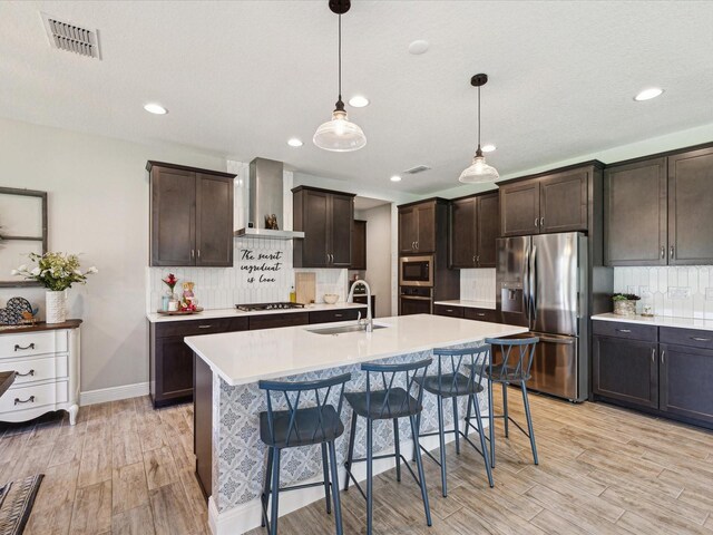 kitchen with appliances with stainless steel finishes, a sink, light countertops, wall chimney exhaust hood, and visible vents