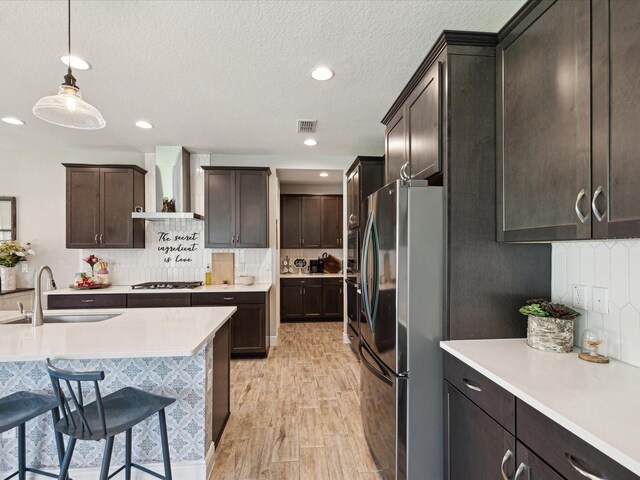kitchen with wall chimney range hood, dark brown cabinetry, a sink, light countertops, and stainless steel appliances