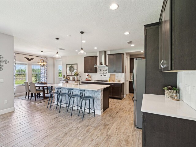 kitchen with light countertops, a breakfast bar, stainless steel appliances, wall chimney exhaust hood, and an island with sink