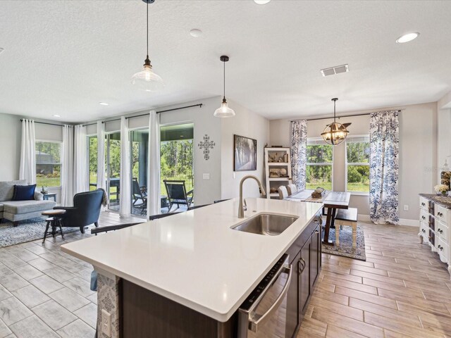 kitchen featuring stainless steel dishwasher, visible vents, a kitchen island with sink, open floor plan, and a sink