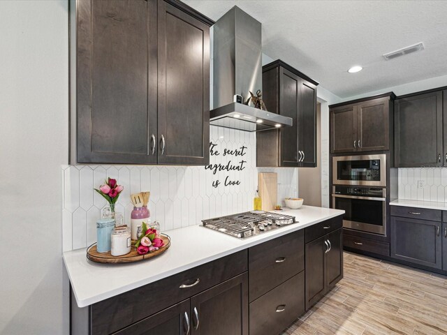 kitchen featuring visible vents, decorative backsplash, light countertops, wall chimney exhaust hood, and appliances with stainless steel finishes