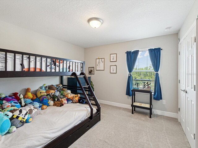 bedroom featuring baseboards, a closet, a textured ceiling, and light colored carpet