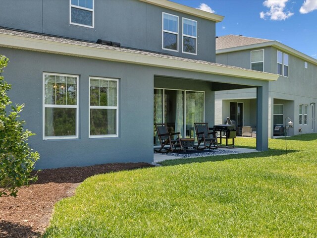 rear view of property featuring a patio area, stucco siding, a yard, and roof with shingles