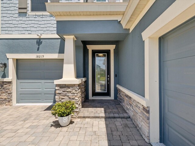 doorway to property with a garage, stucco siding, and stone siding
