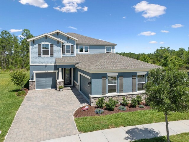 view of front of home with a shingled roof, stucco siding, driveway, and stone siding