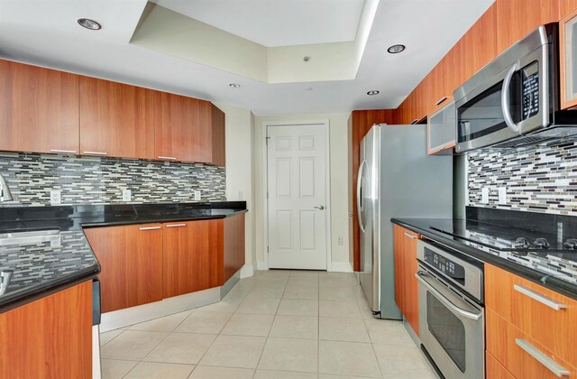 241 Riverside Dr Unit 1107, Daytona Beach, FL 32117 - kitchen with a raised ceiling, brown cabinets, backsplash, and stainless steel appliances