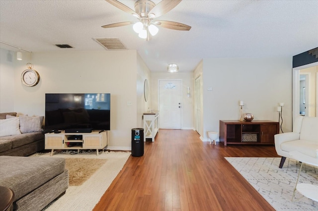 living room featuring visible vents, a textured ceiling, ceiling fan, and wood finished floors