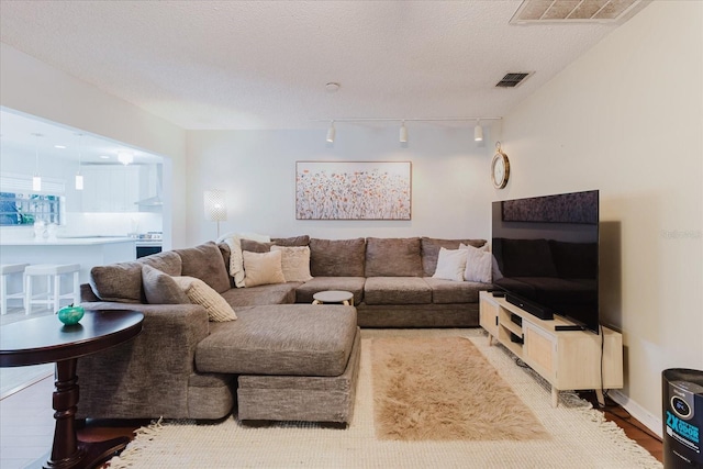 living area featuring track lighting, a textured ceiling, wood finished floors, and visible vents