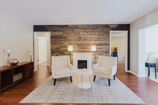 sitting room featuring dark wood-style flooring, a textured ceiling, a glass covered fireplace, and an accent wall