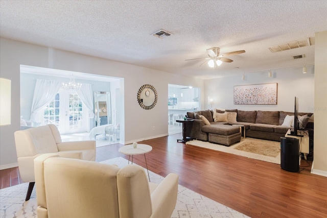 living area with baseboards, visible vents, wood finished floors, and ceiling fan with notable chandelier