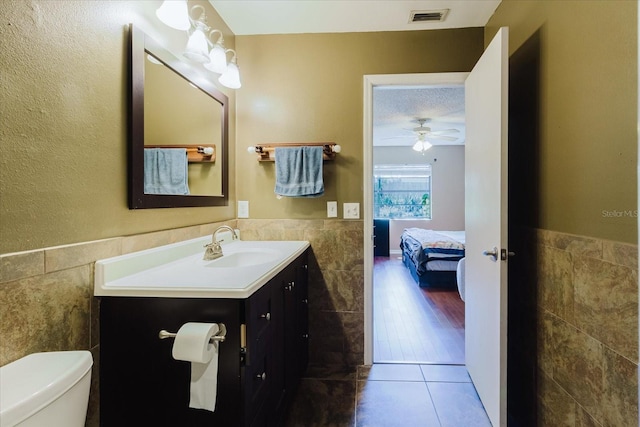 half bathroom featuring visible vents, a wainscoted wall, toilet, and tile walls