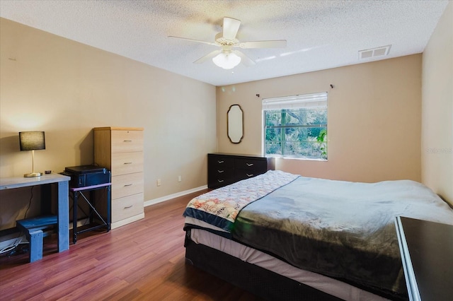 bedroom featuring visible vents, baseboards, a textured ceiling, and wood finished floors