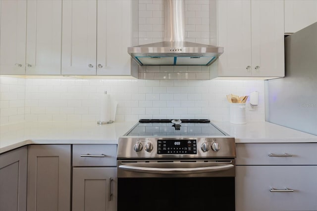 kitchen with wall chimney range hood, backsplash, light countertops, and stainless steel range with electric stovetop