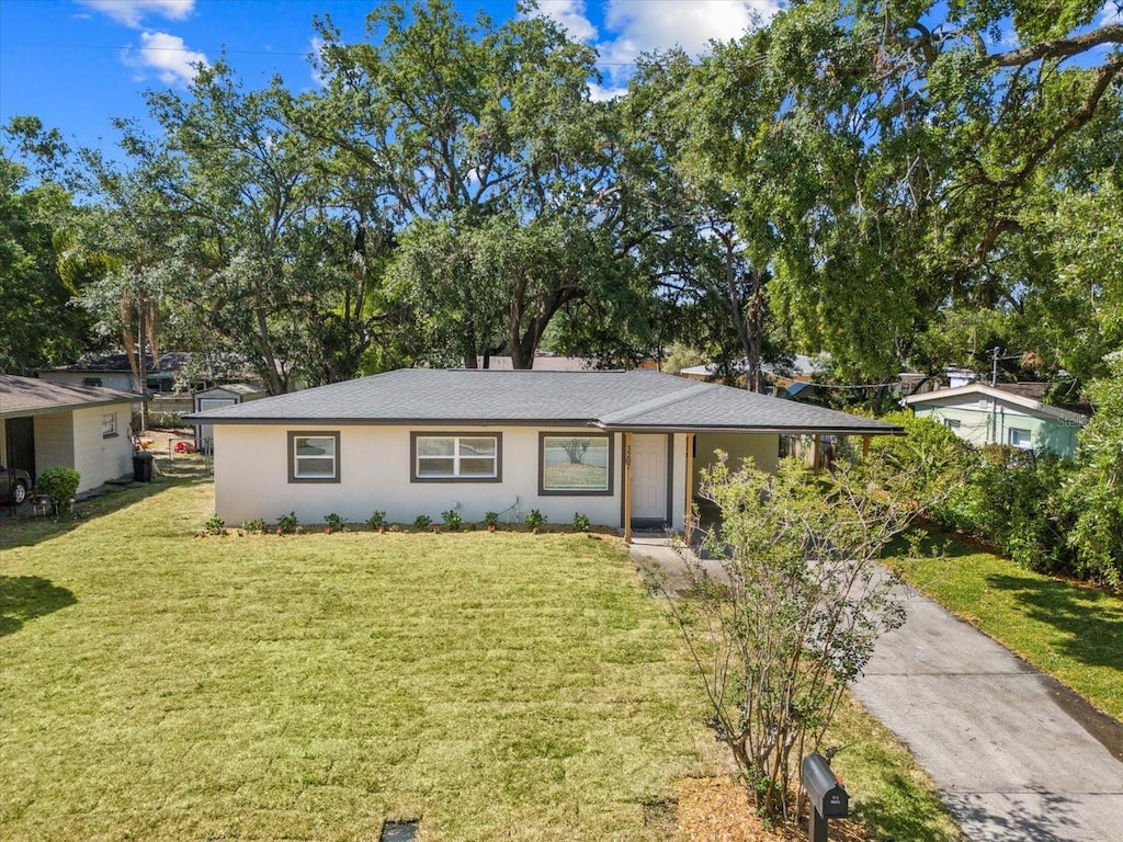 ranch-style home featuring stucco siding, a front yard, and roof with shingles