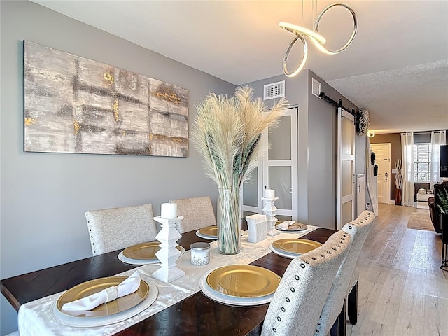 dining area featuring wood finished floors, a barn door, and visible vents