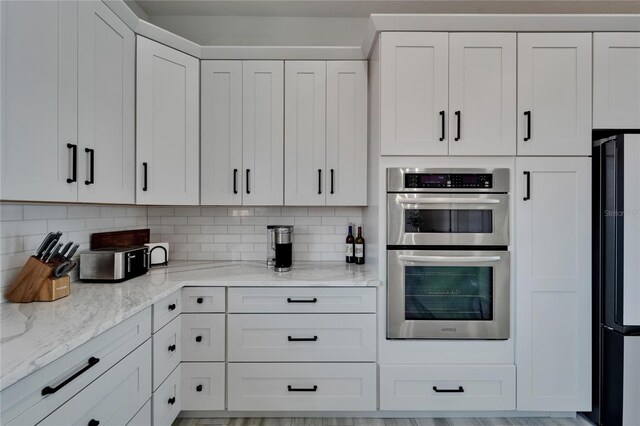 935 Chipaway Dr, Apollo Beach, FL 33572 - kitchen featuring stainless steel double oven, freestanding refrigerator, backsplash, light stone countertops, and white cabinetry
