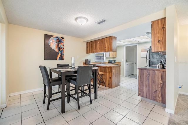 dining space featuring visible vents, baseboards, washer / clothes dryer, a textured ceiling, and light tile patterned floors