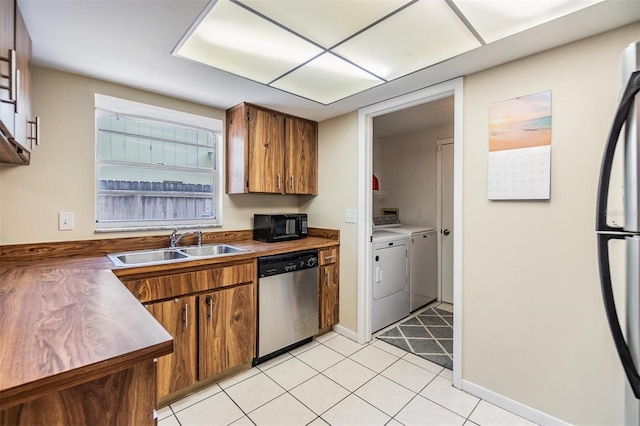 kitchen featuring washing machine and clothes dryer, brown cabinets, a sink, stainless steel appliances, and light tile patterned floors