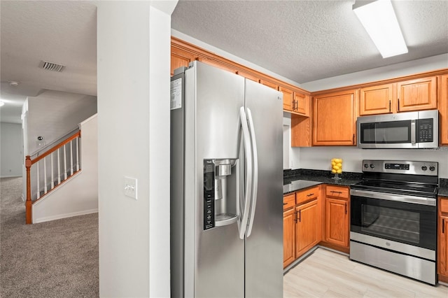 kitchen with brown cabinetry, stainless steel appliances, a textured ceiling, and visible vents