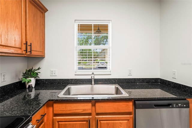 kitchen with brown cabinetry, a sink, dark stone countertops, and stainless steel appliances