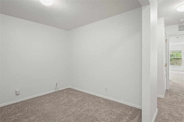spare room featuring baseboards, a textured ceiling, visible vents, and light carpet