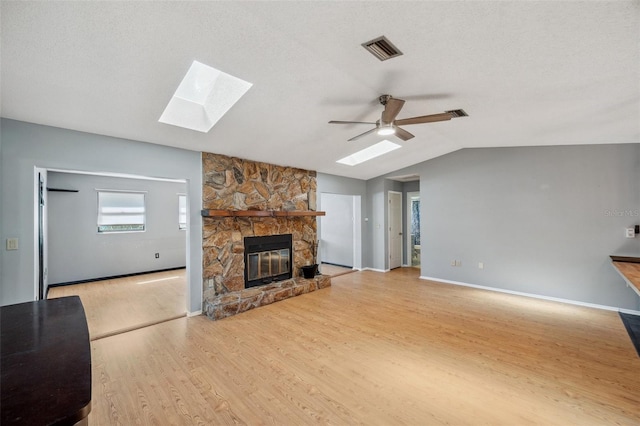 unfurnished living room featuring vaulted ceiling with skylight, a fireplace, ceiling fan, visible vents, and wood finished floors