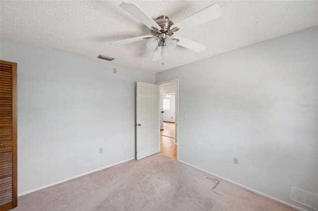 unfurnished room with a ceiling fan, visible vents, light carpet, and baseboards