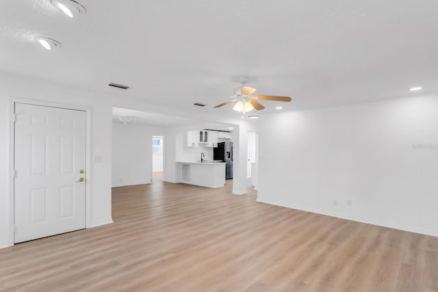 unfurnished living room with a sink, visible vents, ceiling fan, and light wood-type flooring