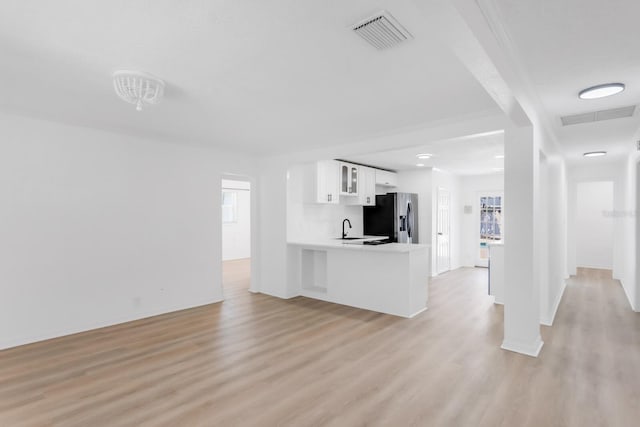 unfurnished living room with baseboards, visible vents, light wood-style flooring, and a sink