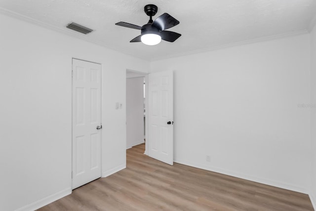 unfurnished bedroom with light wood-type flooring, a ceiling fan, visible vents, baseboards, and ornamental molding