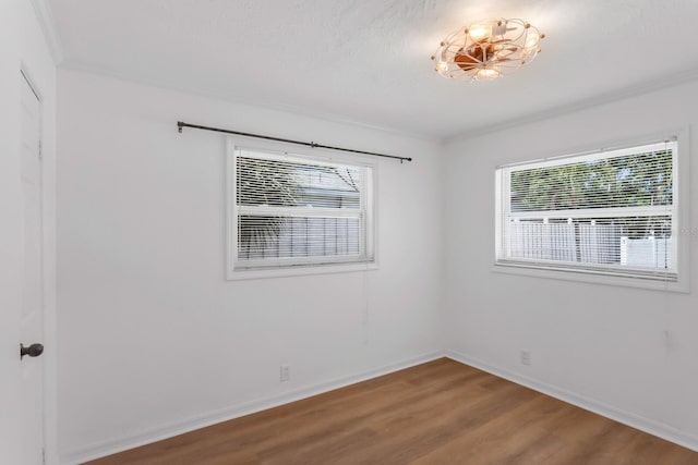 spare room with a wealth of natural light, wood finished floors, crown molding, and baseboards