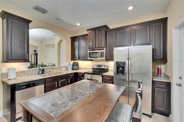 kitchen featuring visible vents, dark brown cabinetry, arched walkways, a sink, and stainless steel appliances
