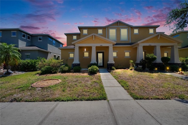 craftsman-style house with covered porch, stucco siding, and a yard