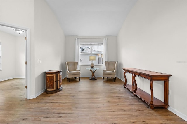 living area with baseboards, vaulted ceiling, and light wood-type flooring