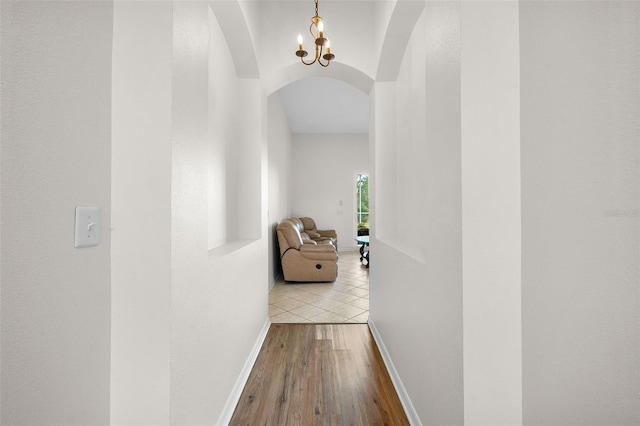 corridor with arched walkways, a notable chandelier, wood finished floors, and baseboards