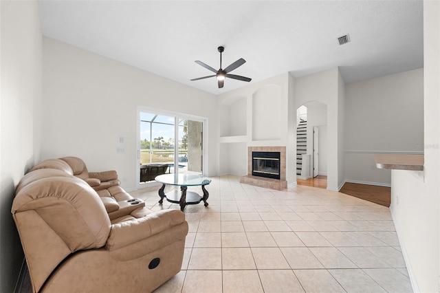 living area with light tile patterned floors, visible vents, arched walkways, a tiled fireplace, and a ceiling fan