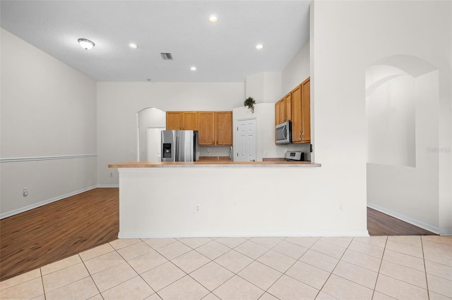 kitchen with appliances with stainless steel finishes, brown cabinets, recessed lighting, and arched walkways