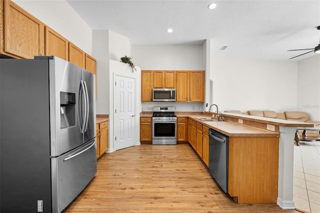 kitchen featuring stainless steel appliances, a sink, light wood-type flooring, a peninsula, and open floor plan