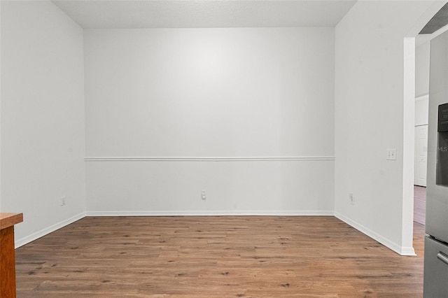 unfurnished room featuring baseboards, wood finished floors, and arched walkways