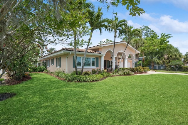 mediterranean / spanish-style house featuring stucco siding, a front yard, a tiled roof, and an attached garage