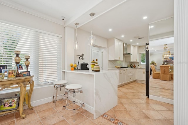kitchen with a peninsula, wall chimney range hood, light countertops, white cabinetry, and pendant lighting