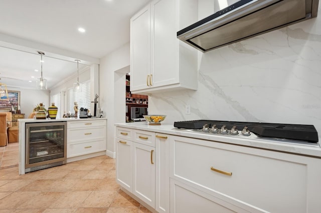 kitchen with beverage cooler, stainless steel gas stovetop, extractor fan, light countertops, and white cabinetry
