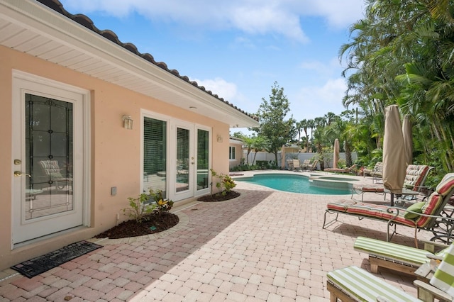 view of pool with a pool with connected hot tub, fence, french doors, and a patio area