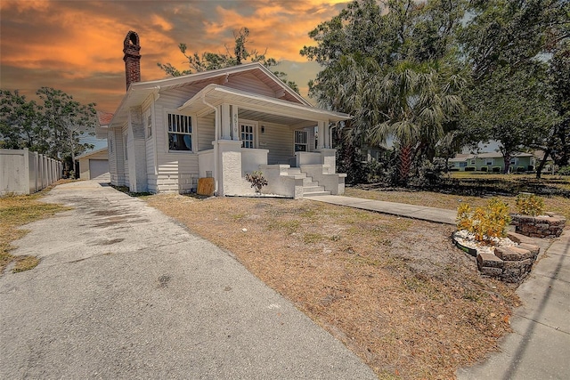 bungalow-style house with fence, a chimney, a detached garage, and a porch