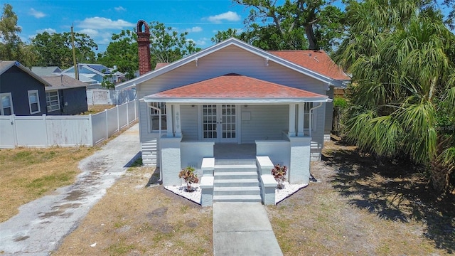 bungalow-style home featuring covered porch, driveway, a chimney, french doors, and fence