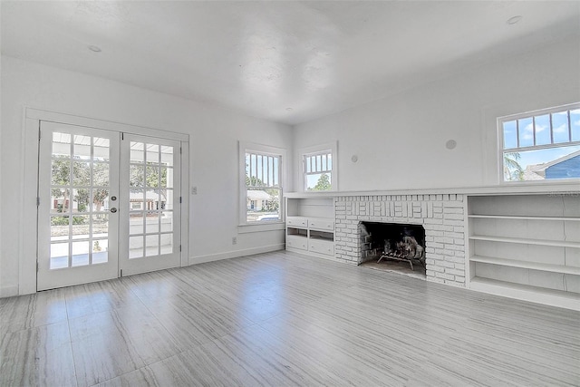 unfurnished living room featuring baseboards, wood finished floors, french doors, and a brick fireplace