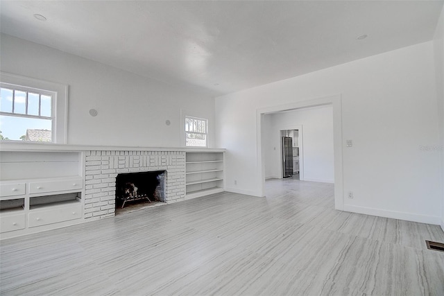 unfurnished living room with baseboards, visible vents, wood finished floors, and a brick fireplace